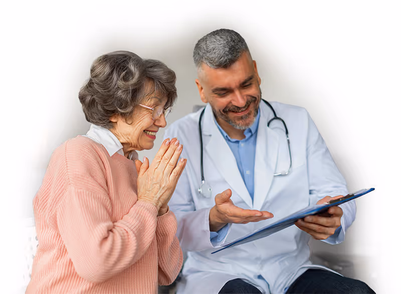 Smiling elderly woman in a pink sweater listening to a male doctor explaining medical information on a clipboard.
