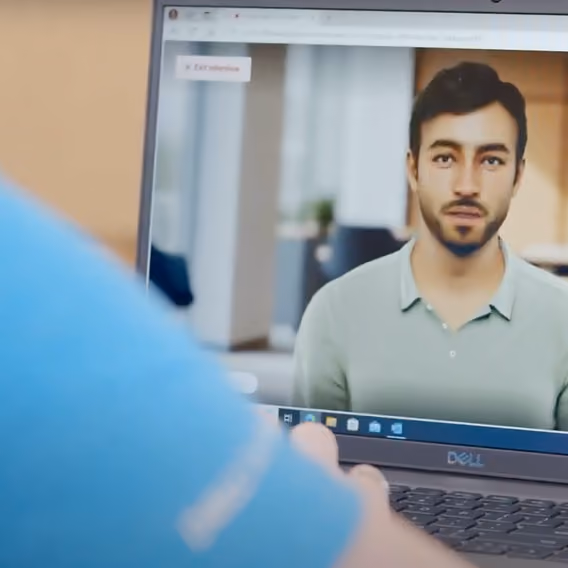 Person in blue shirt interacting with a lifelike virtual human displayed on a Dell laptop screen in an indoor setting.