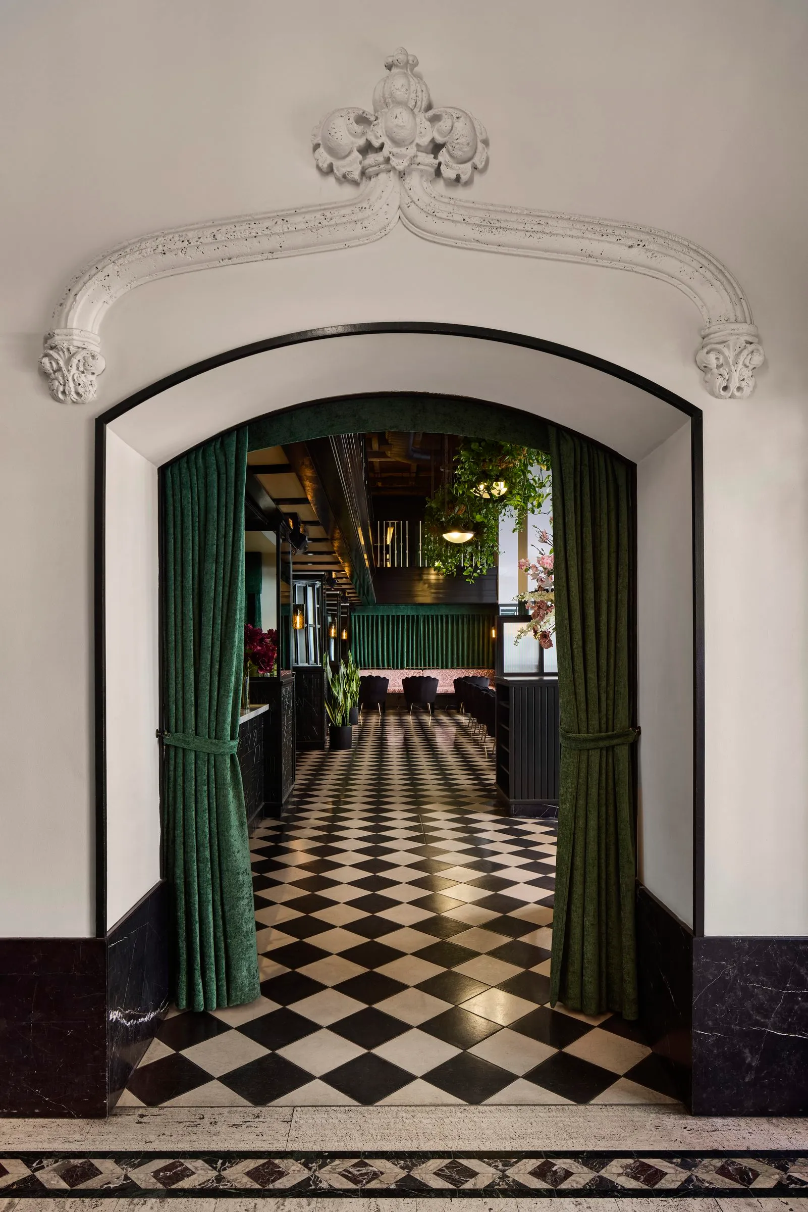An arched entry with ornate white molding and green velvet curtains tied back opens onto Mary at the Stile Hotel.