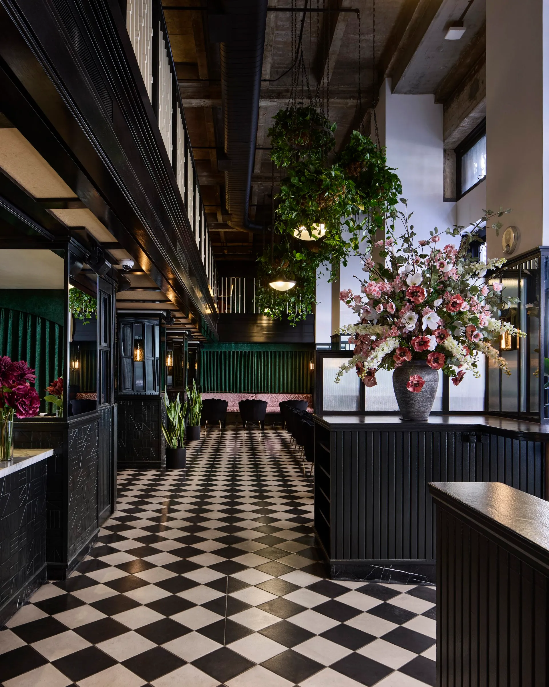 Hanging plants and a large pink floral arrangement beside a checkered tile aisle at Mary at the Stile Hotel by day.