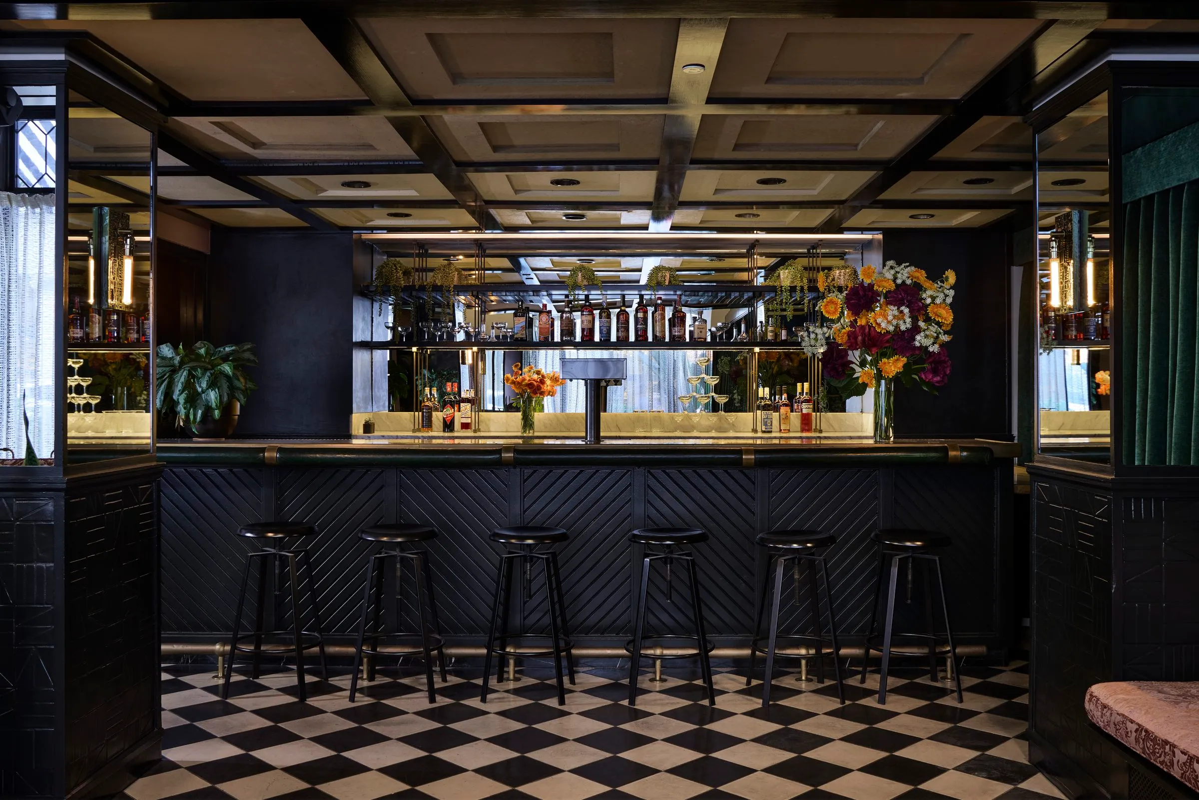The bar with six black stools and shelves of bottles under a coffered ceiling at Mary at the Stile Hotel.