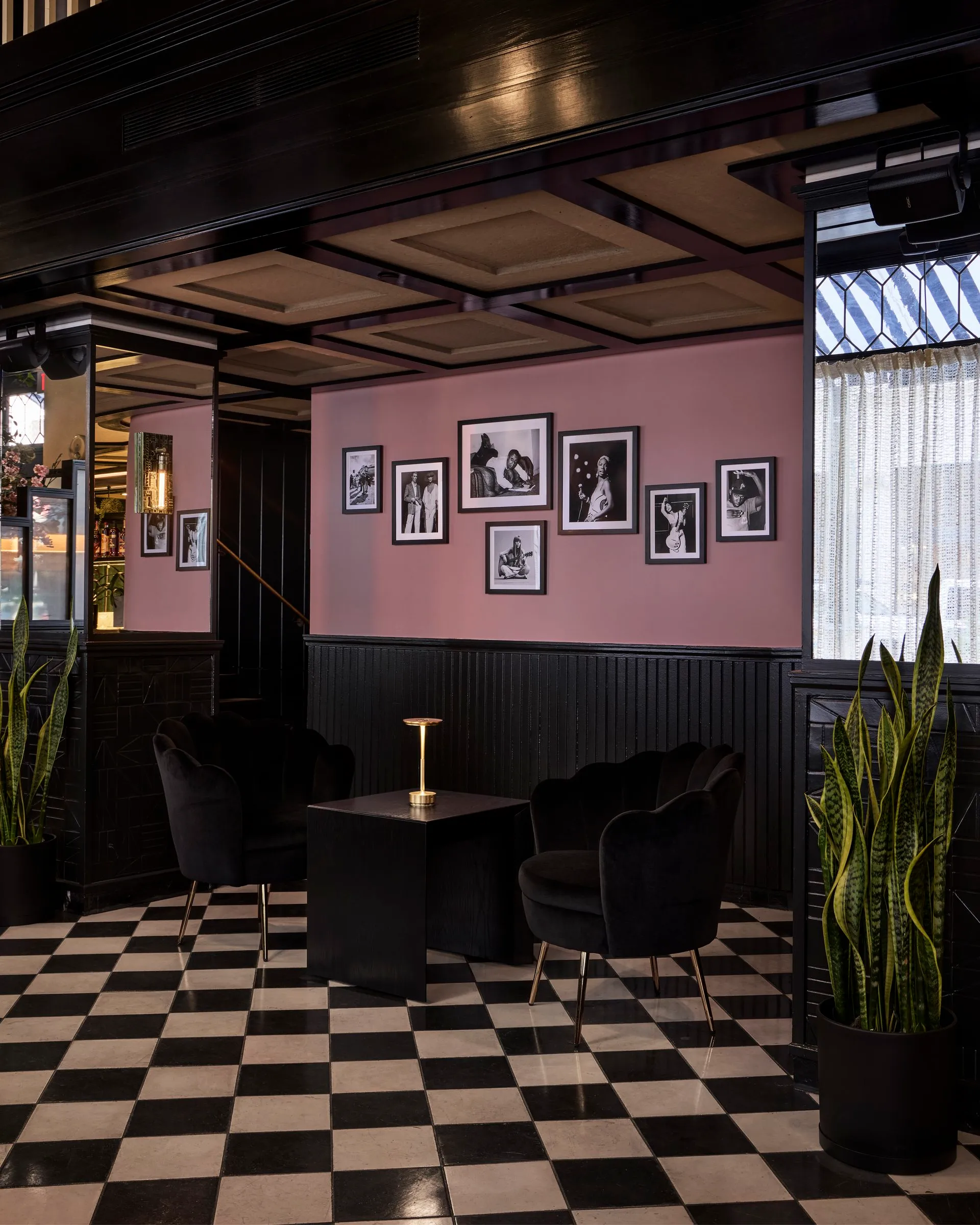 Framed black and white photos on a pink wall over dark wainscoting and two scalloped chairs at Mary at the Stile Hotel.
