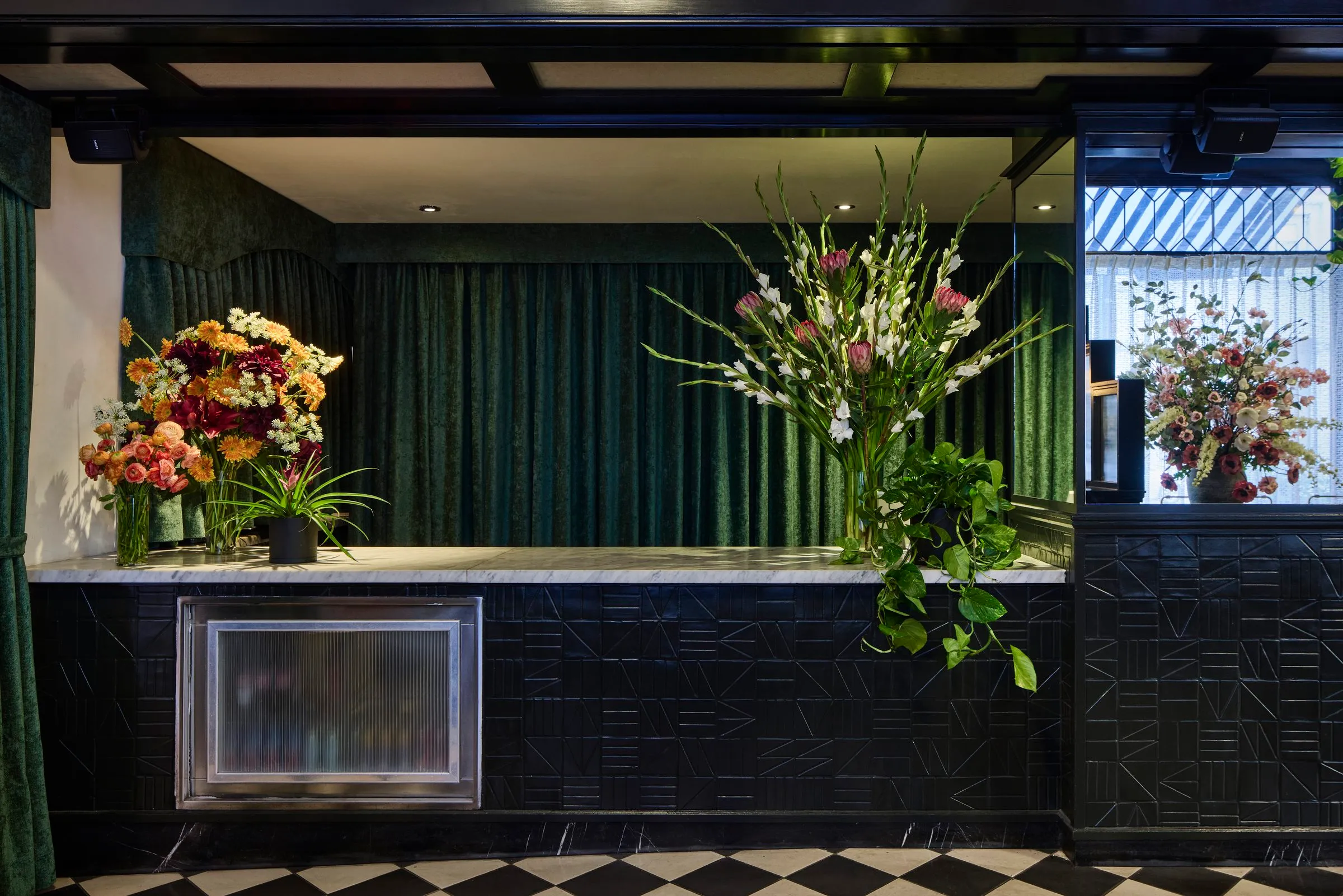 Flowers on a white counter with a carved black front, backed by green velvet curtains, at Mary at the Stile Hotel.