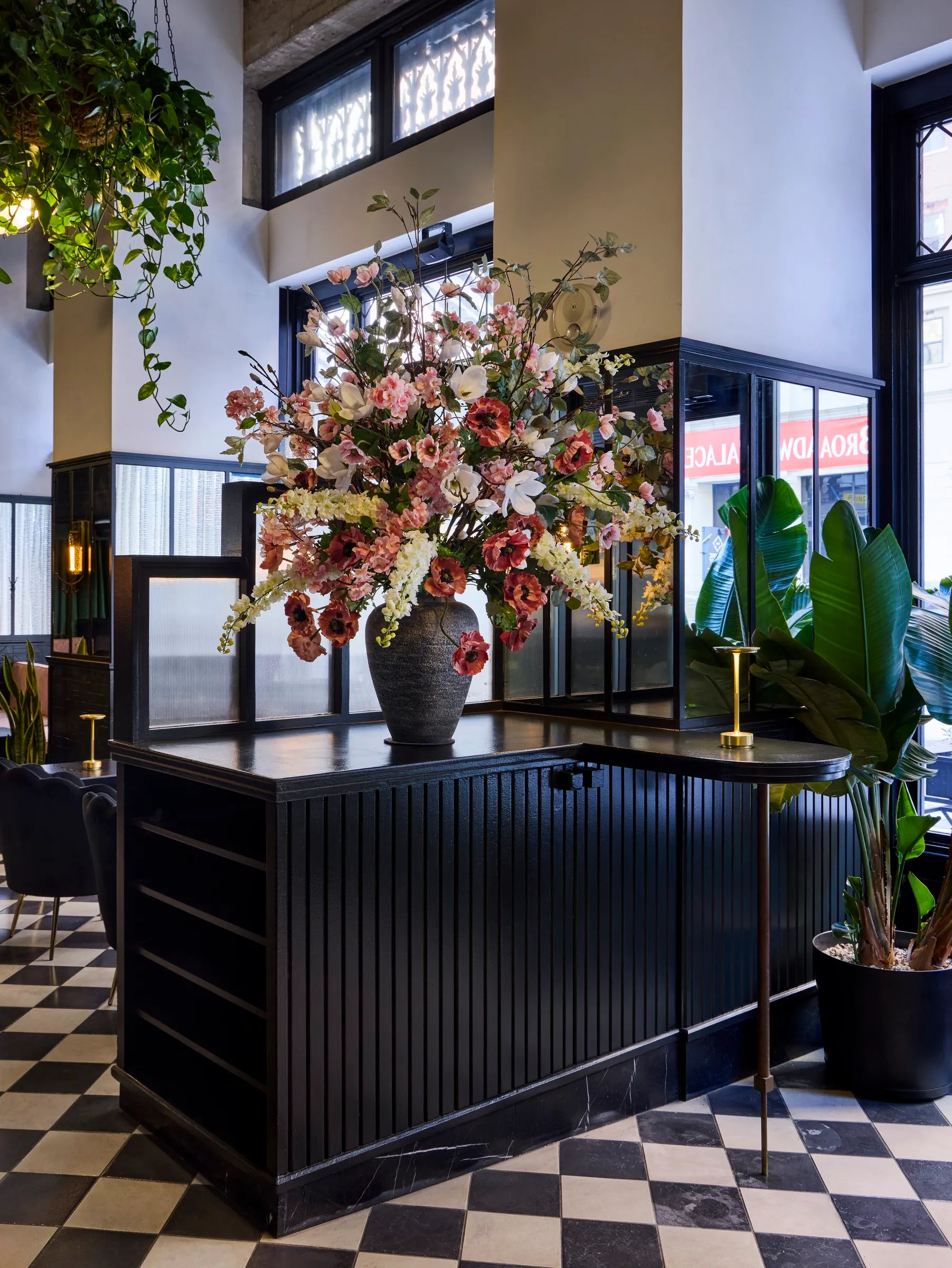 A large pink and white floral arrangement on a dark paneled counter above checkered tile at Mary at the Stile Hotel.