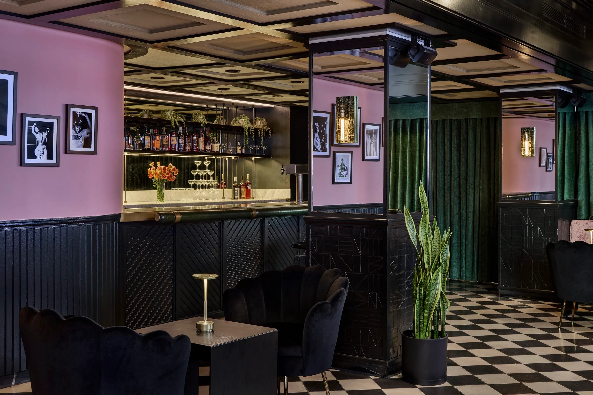 Pink walls with framed photos, the bar, green velvet curtains and black scalloped chairs at Mary at the Stile Hotel.