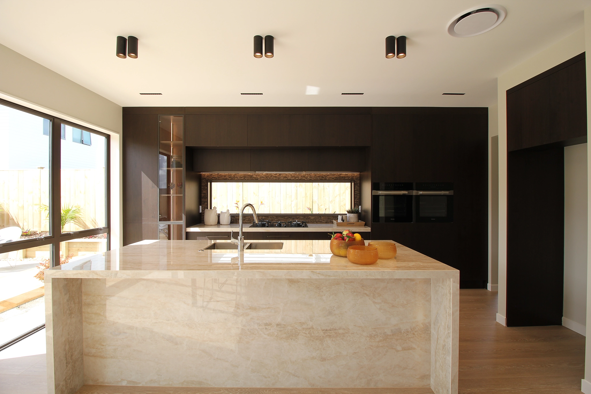 Dark timber joinery island with waterfall edge and push-to-open cabinetry, Auckland