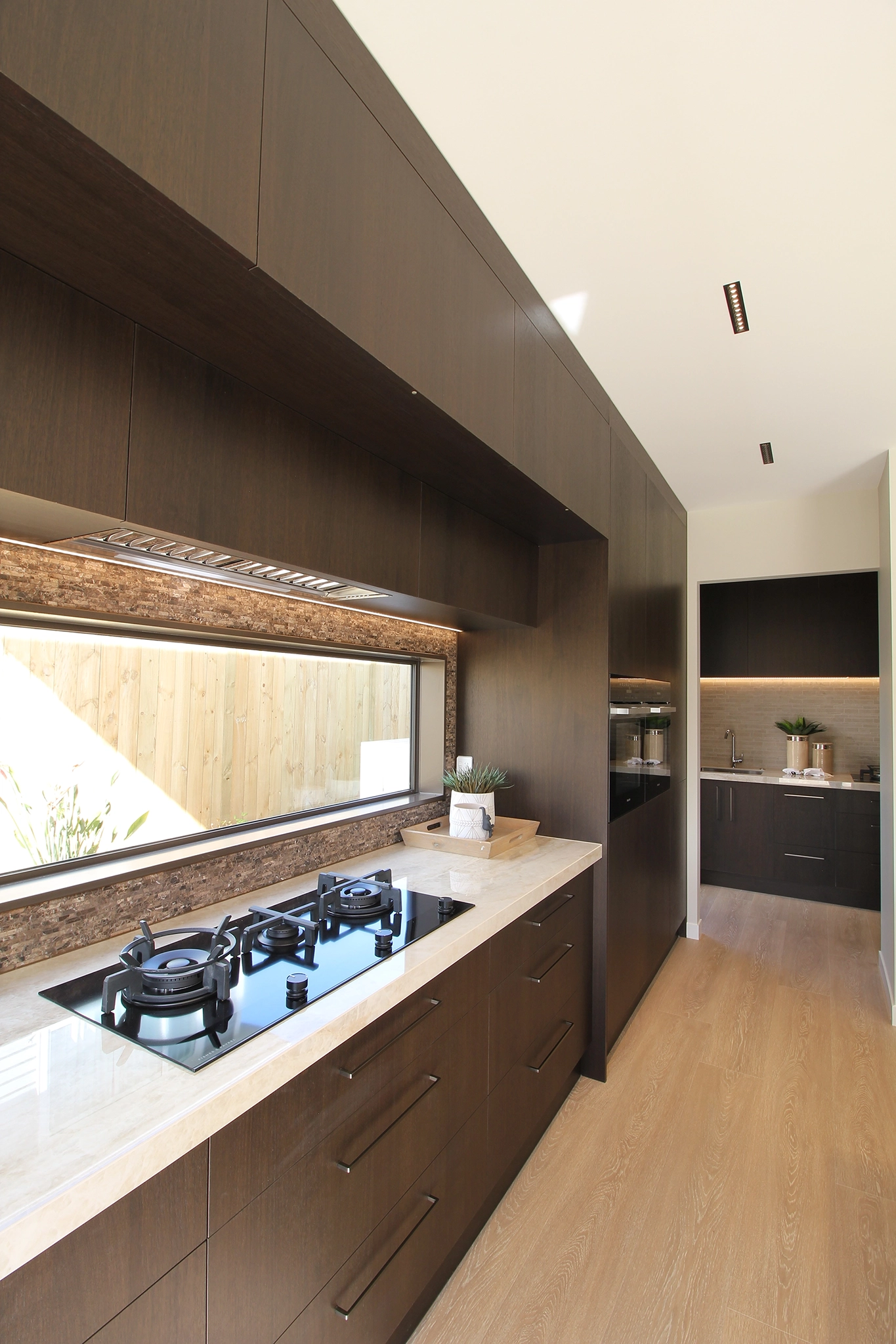 Dark timber joinery with Deep grain Shinnoki veneer in an open-plan kitchen, Pepeke Way, WL Developments