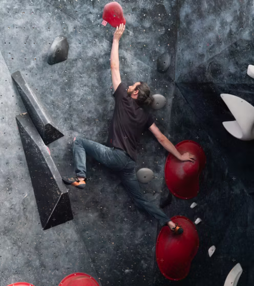 Patrick klettert agil an der Boulderwand und streckt sich gerade nach dem nächsten Griff