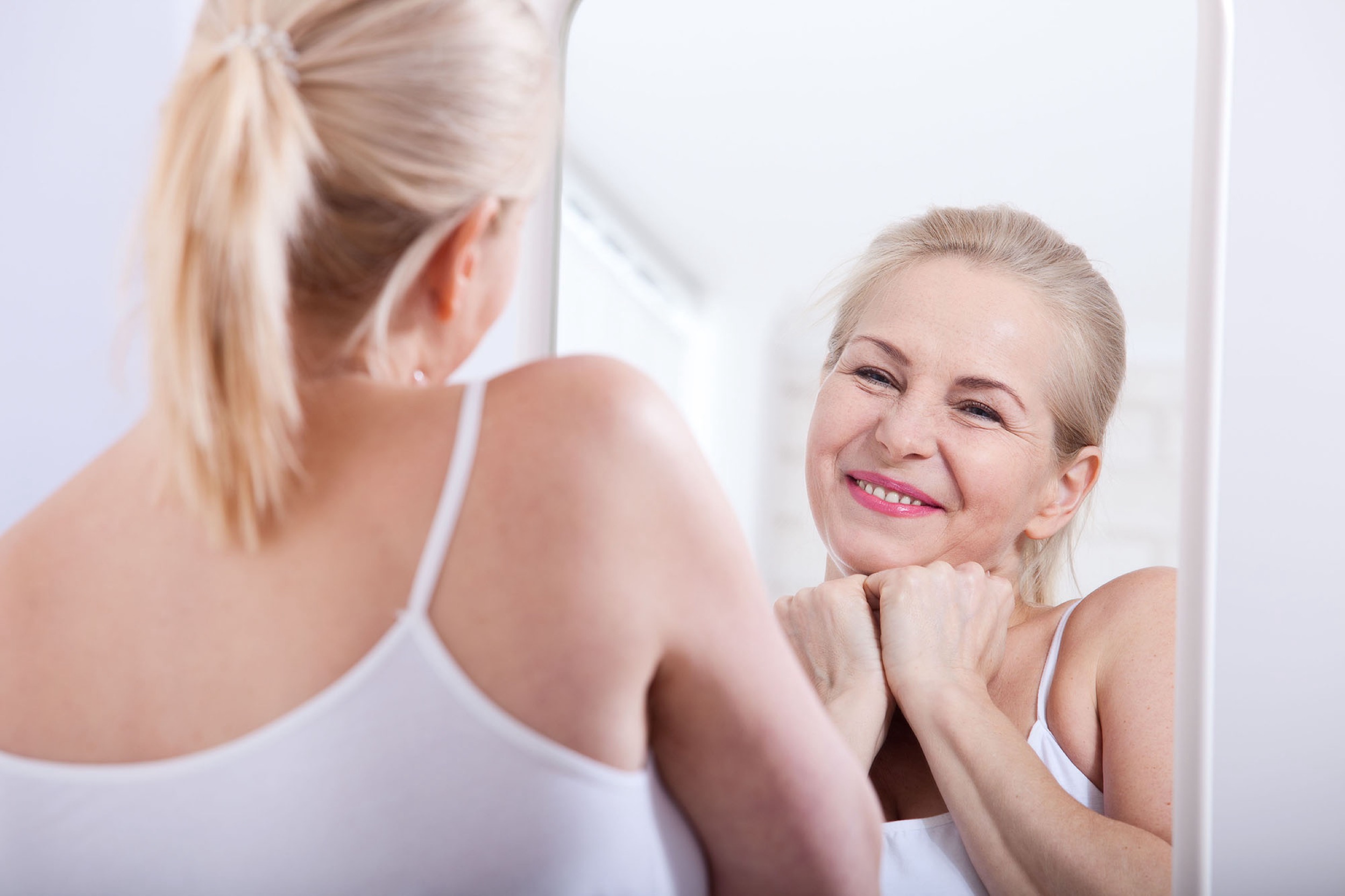 Black-and-white photograph of a woman smiling at her reflection in a mirror