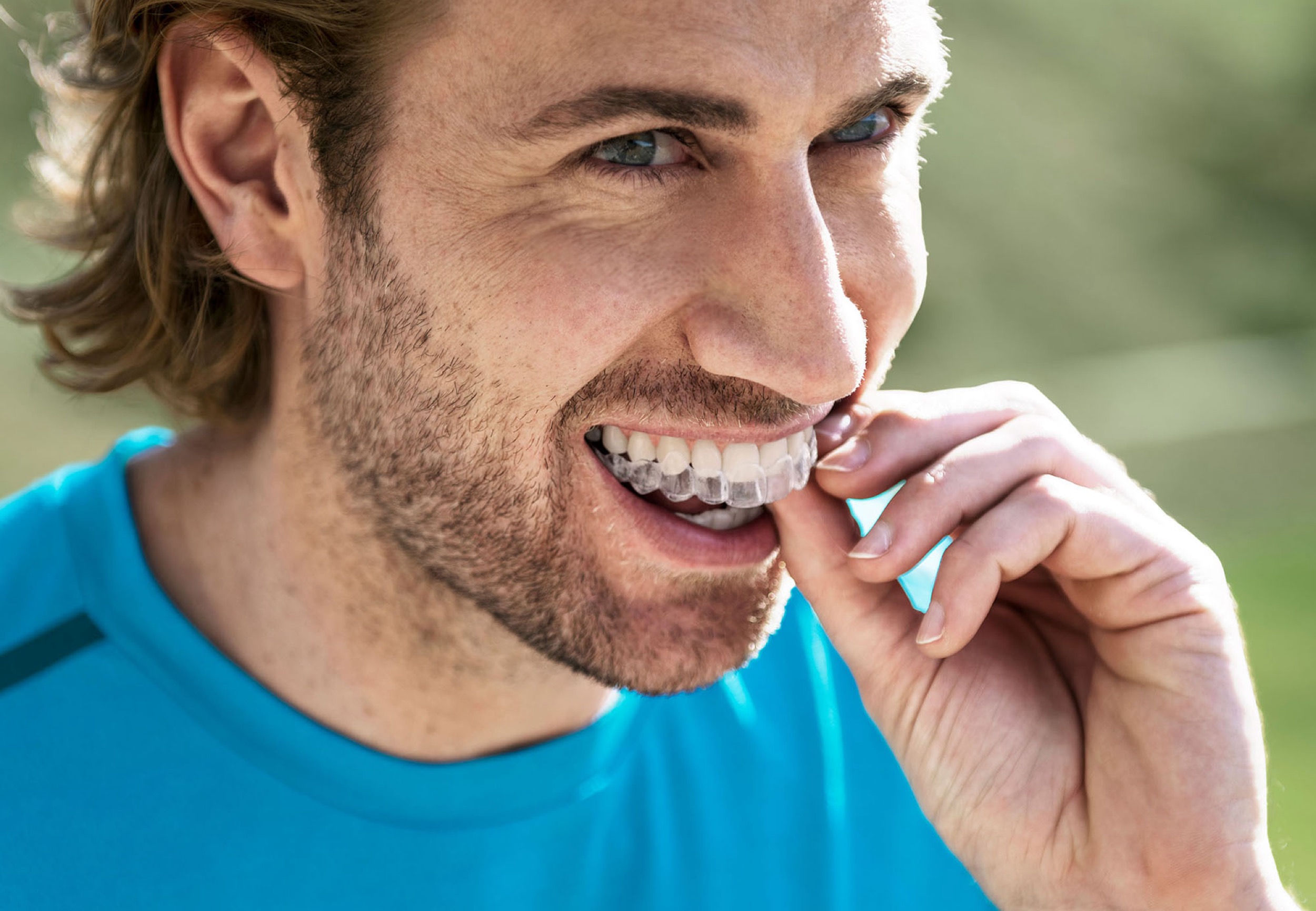 Man smiling while fitting a clear aligner over his teeth