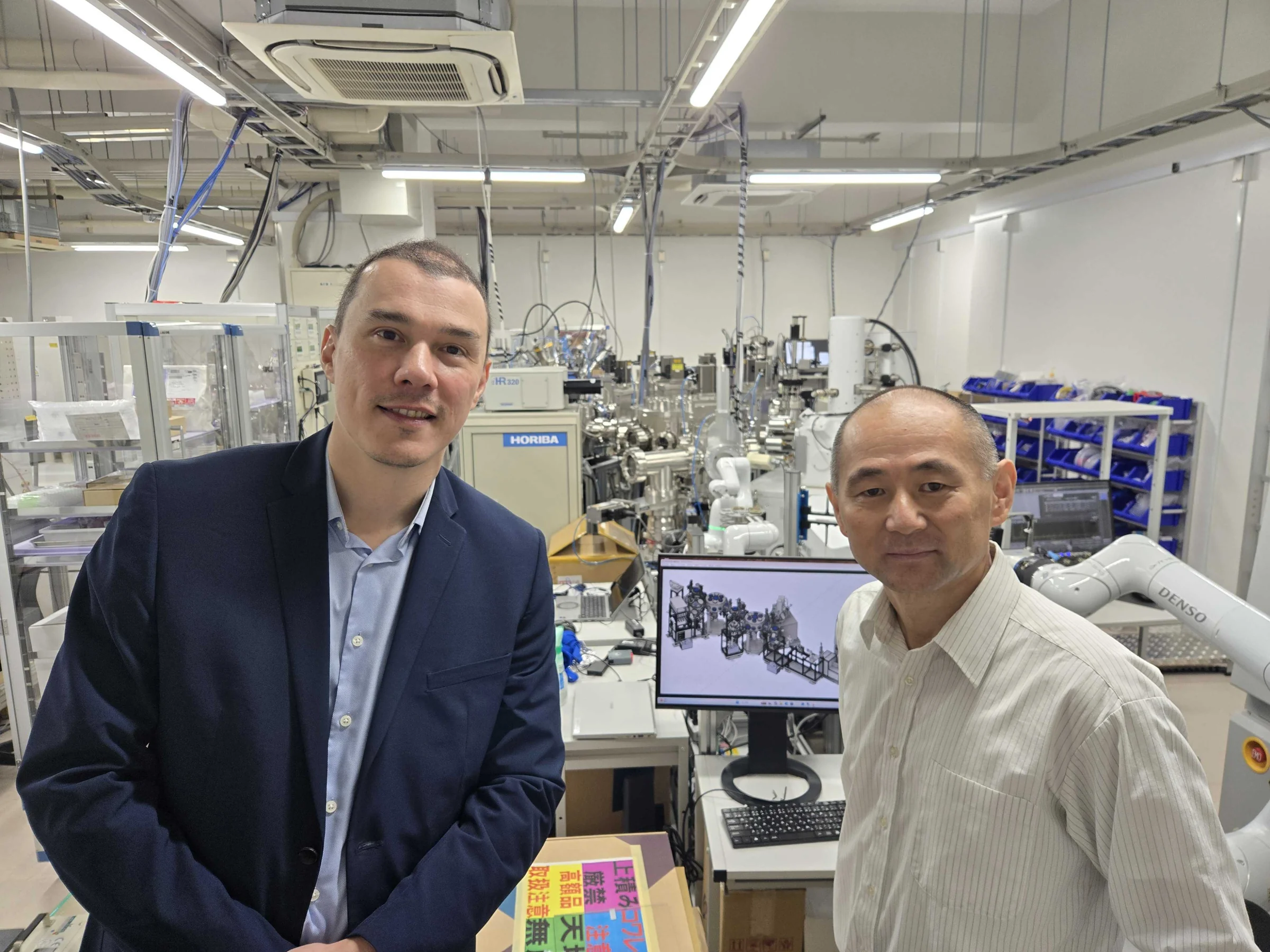 ロボットアームや実験装置が並ぶ研究室で、担当者と並ぶMat3raチームのメンバー