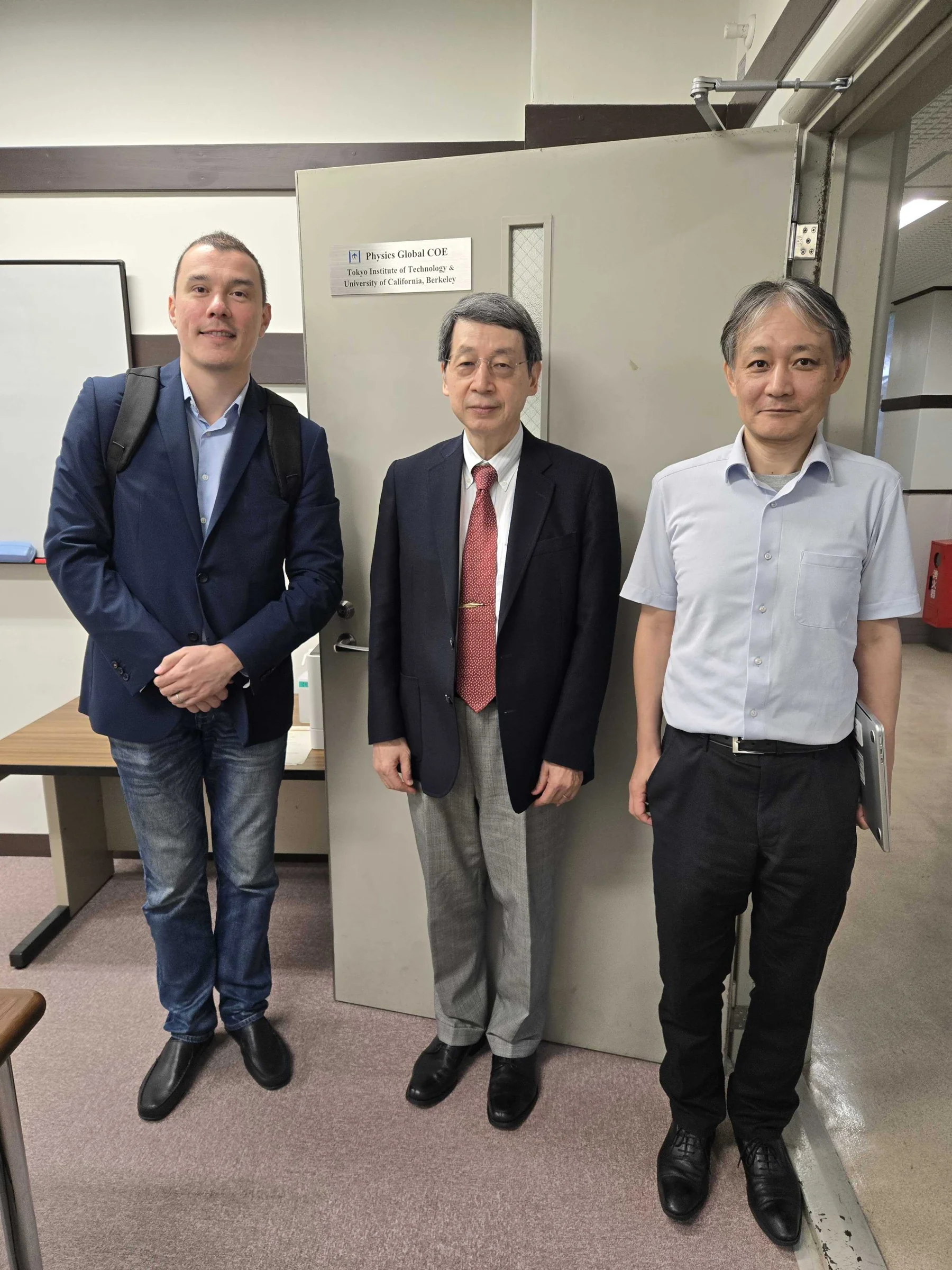 A Mat3ra team member with two hosts at Science Tokyo, in front of a door with a Physics Global COE sign