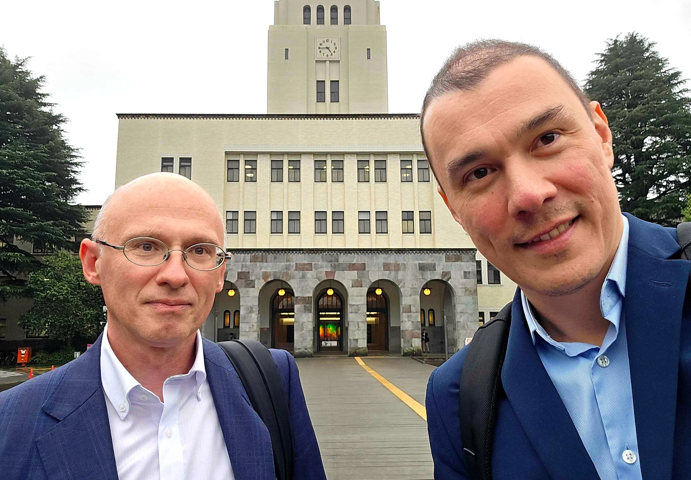 Two members of the Mat3ra team in front of the clock-tower main building at Science Tokyo on an overcast day