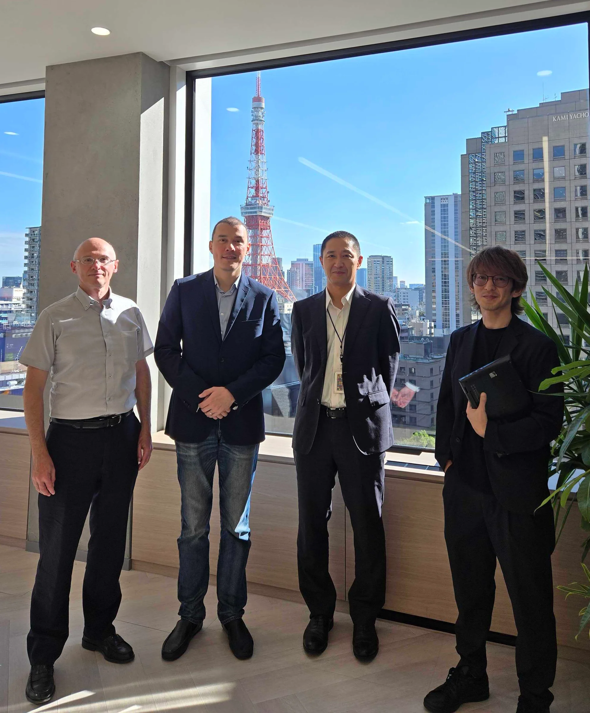 Two members of the Mat3ra team with two hosts in an office with Tokyo Tower visible through the window