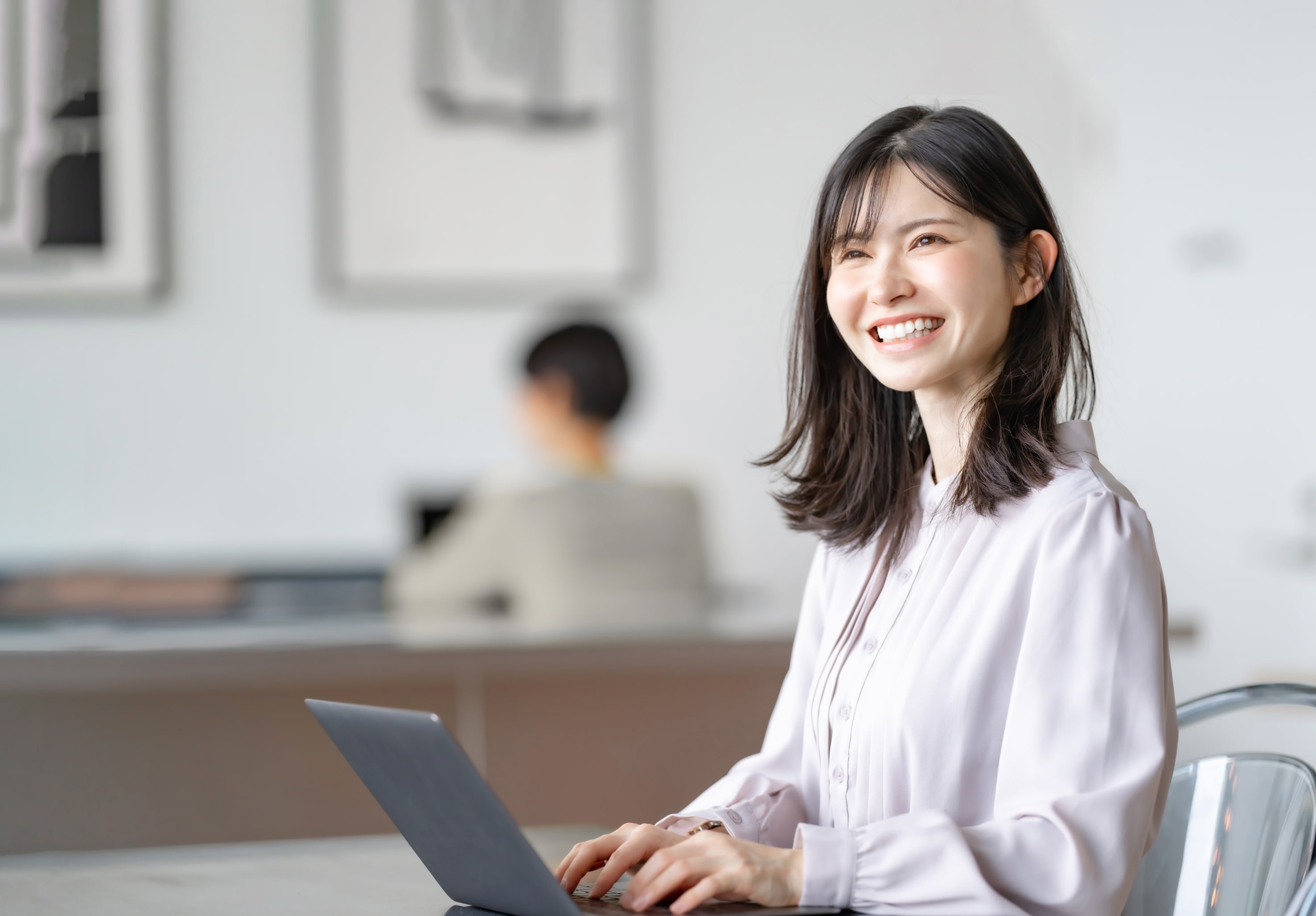 オフィスでノートパソコンにタイピングしながら微笑む若い女性