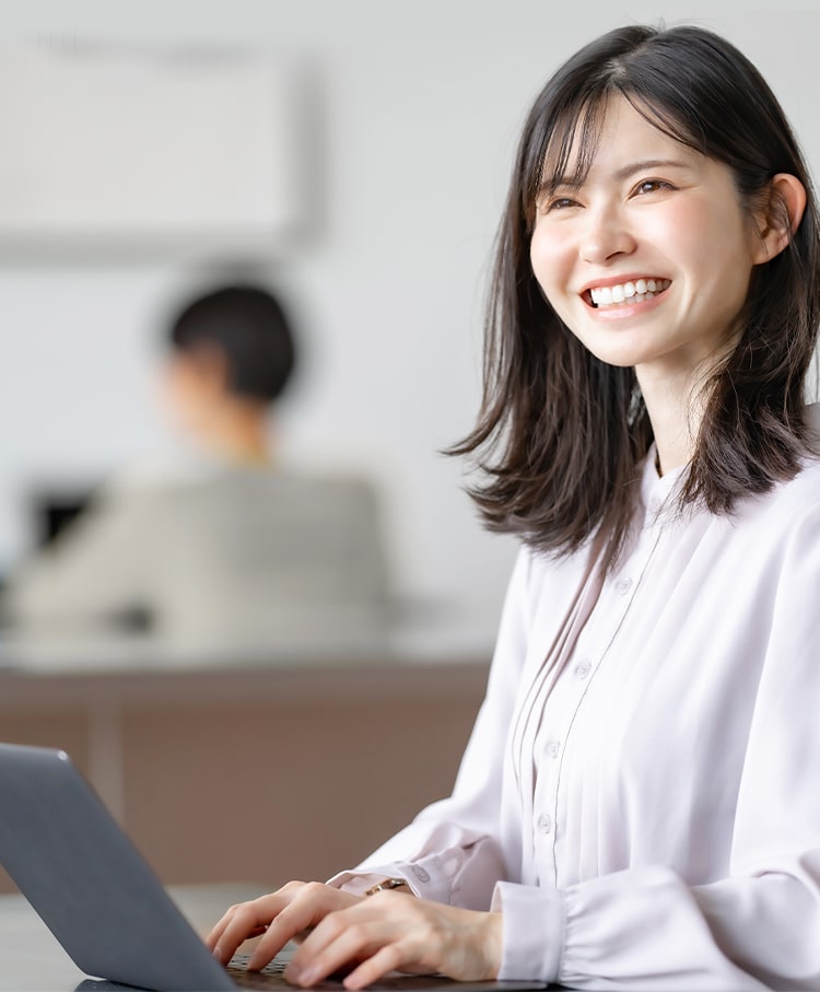 オフィスでノートパソコンにタイピングしながら微笑む若い女性