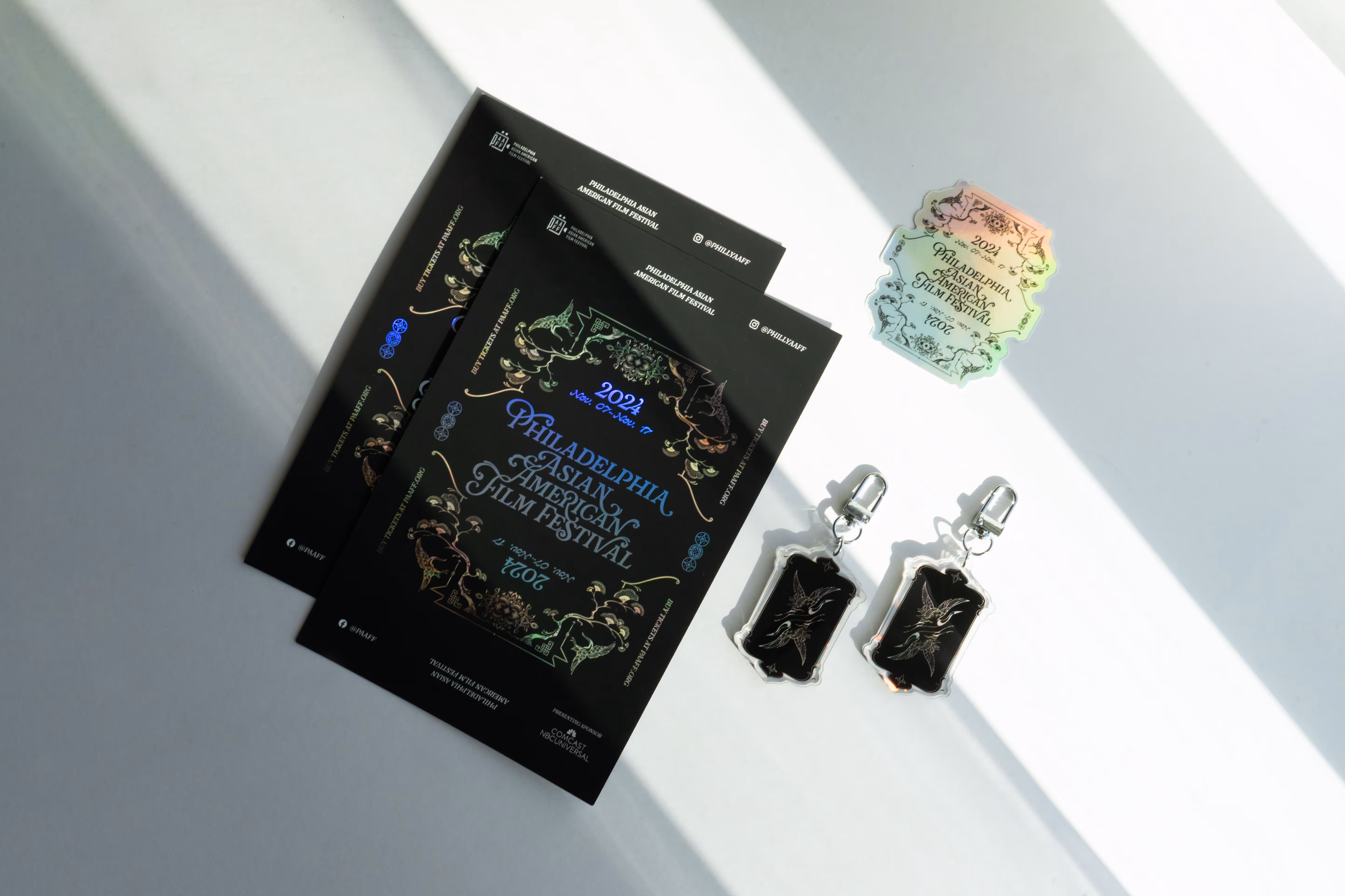 A layout of PAAFF physical takeaways including holographic postcards, stickers, and keychains.