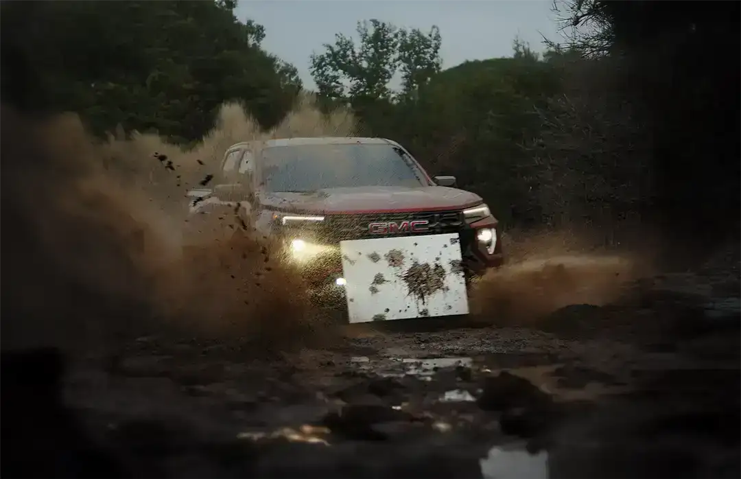 GMC Canyon AT4X kicking up mud while off-roading, with a mounted white canvas collecting splattered mud for the 'Mudern Art' project.