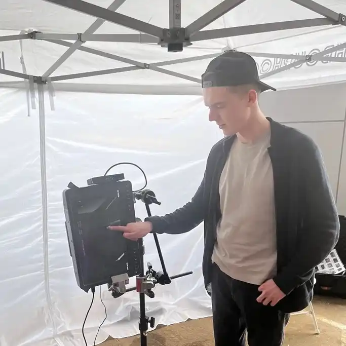 Andrew Reutsky on set, interacting with a monitor under a white canopy, wearing a casual outfit with a backward cap.