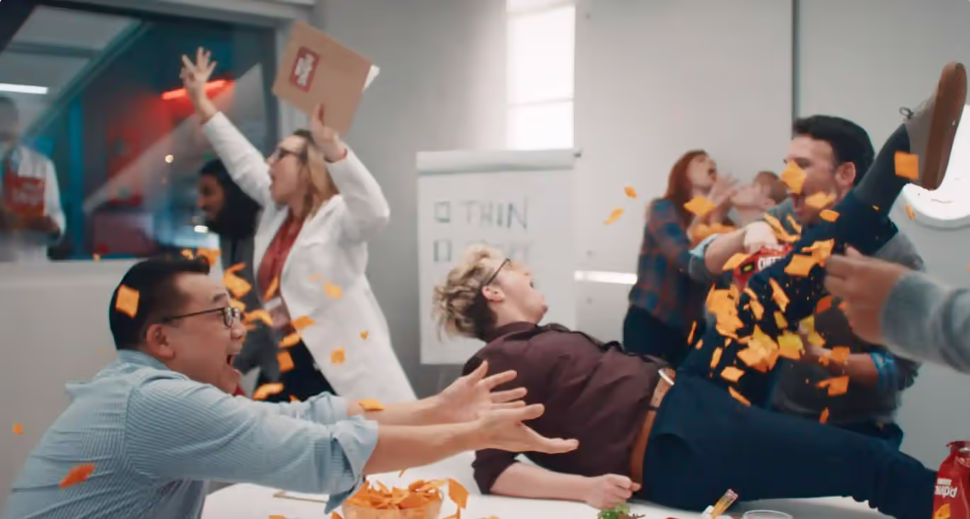 Cheez-It Snap'd launch campaign scene featuring an energetic office celebration with people joyfully tossing cheesy snacks in the air.