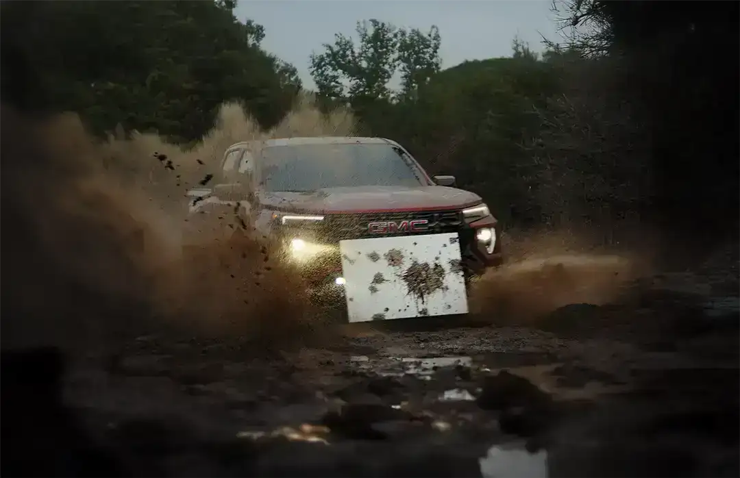 GMC Canyon AT4X мчится по грязи, поднимая брызги, на переднем бампере закреплен белый холст с пятнами грязи — арт-инсталляция Mudern Art.