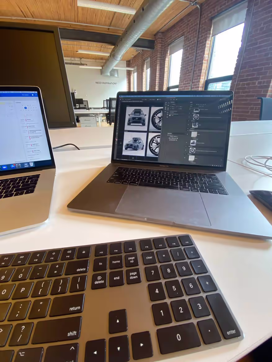 MacBook running Photoshop with Volvo ad assets in a loft-style brick office.