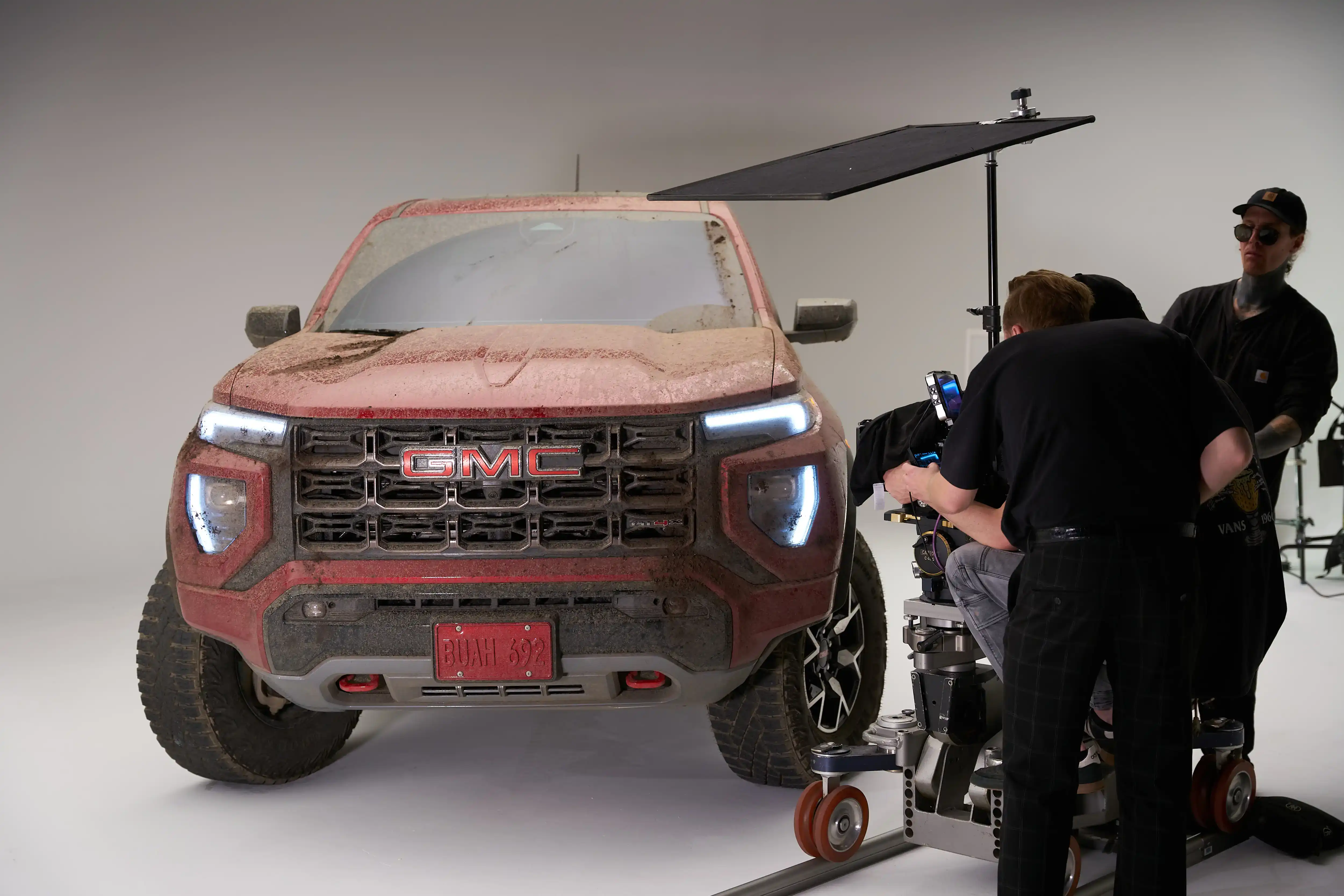 Mud-covered GMC Sierra AT4X on a white-cyclorama set while the crew films a commercial.