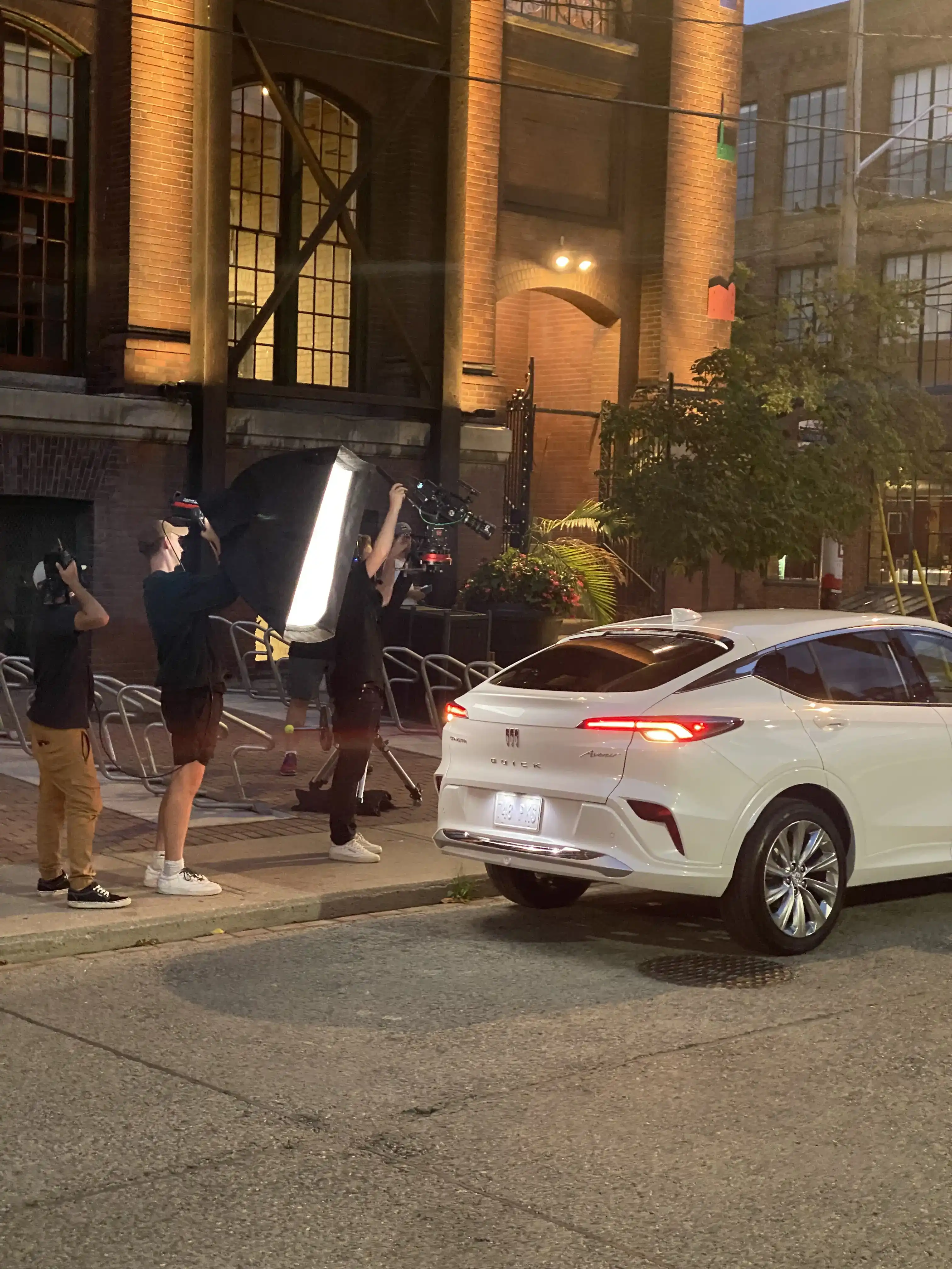 Film crew lights a white Buick Envista during a nighttime street commercial shoot.