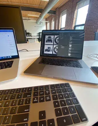 打开 Photoshop 设计沃尔沃创意稿的 MacBook,位于砖墙开放式办公室。