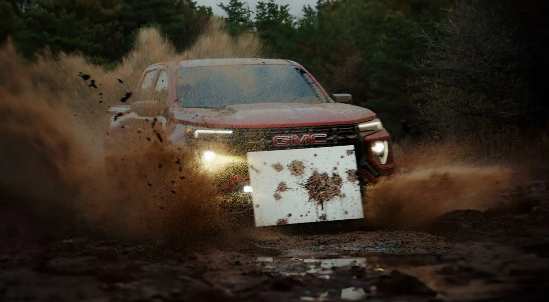 <GMC Canyon AT4X kicking up mud while off-roading, with a mounted white canvas collecting splattered mud for the 'Mudern Art' project.>