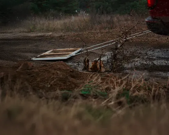 A GMC vehicle drives along a muddy dirt road while pulling a canvas attached by ropes, creating another mud masterpiece.