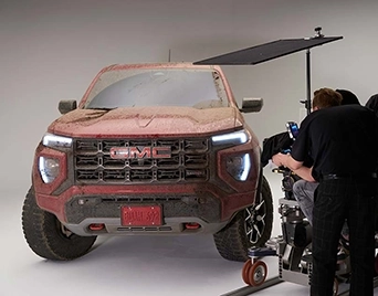 Mud-covered GMC Sierra AT4X on a white-cyclorama set while the crew films a commercial.