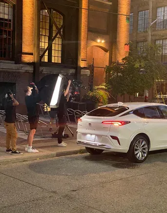 Film crew lights a white Buick Envista during a nighttime street commercial shoot.