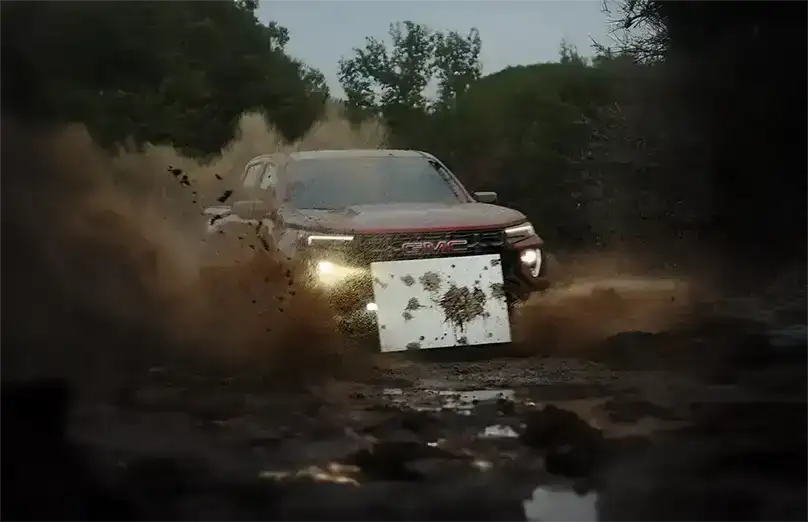 GMC Canyon AT4X kicking up mud while off-roading, with a mounted white canvas collecting splattered mud for the 'Mudern Art' project.