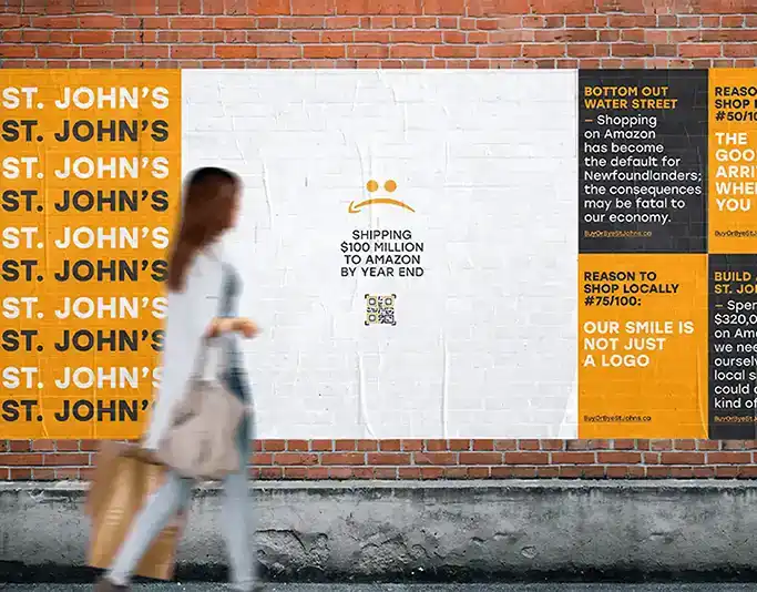 A campaign poster on a brick wall showing messages about local shopping in St. John’s and Amazon spending.