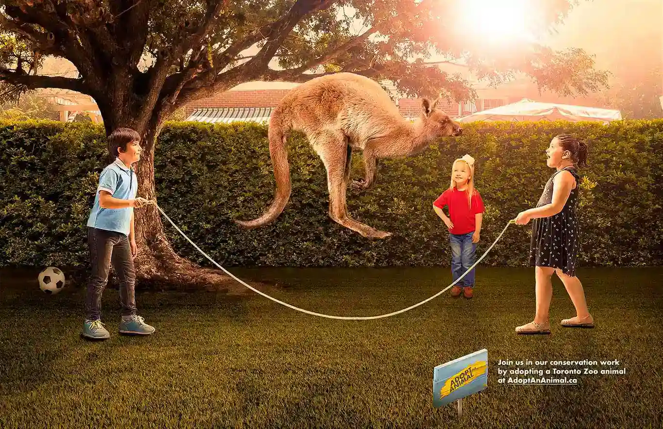 <Children stand on a grassy lawn holding a rope in a Toronto Zoo 'Adopt an Animal' campaign image, with a kangaroo floating playfully above them in a sunlit backyard setting. >