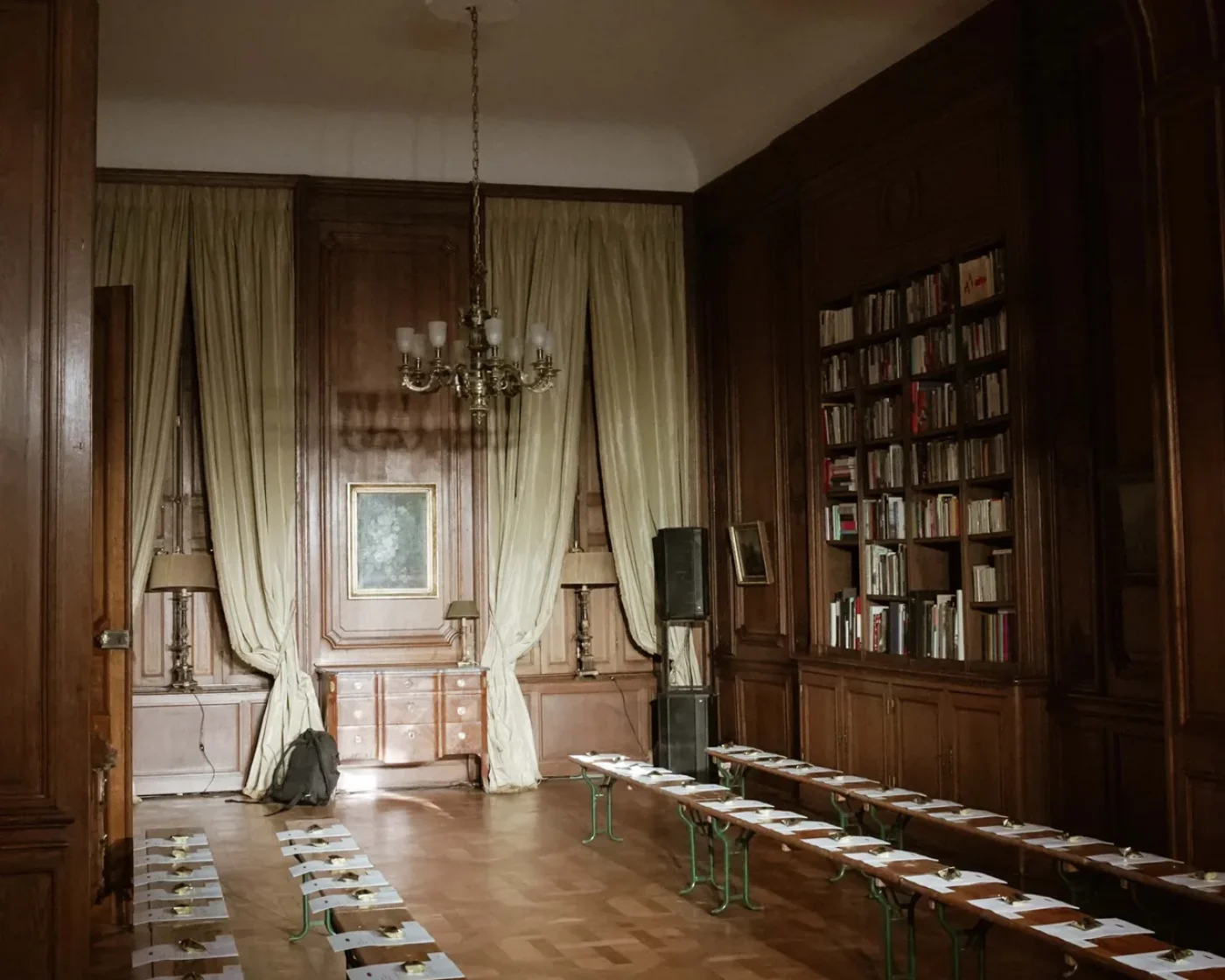 Le salon-bibliothèque vide avant le défilé : bancs alignés, cartons de placement posés, rideaux ouverts