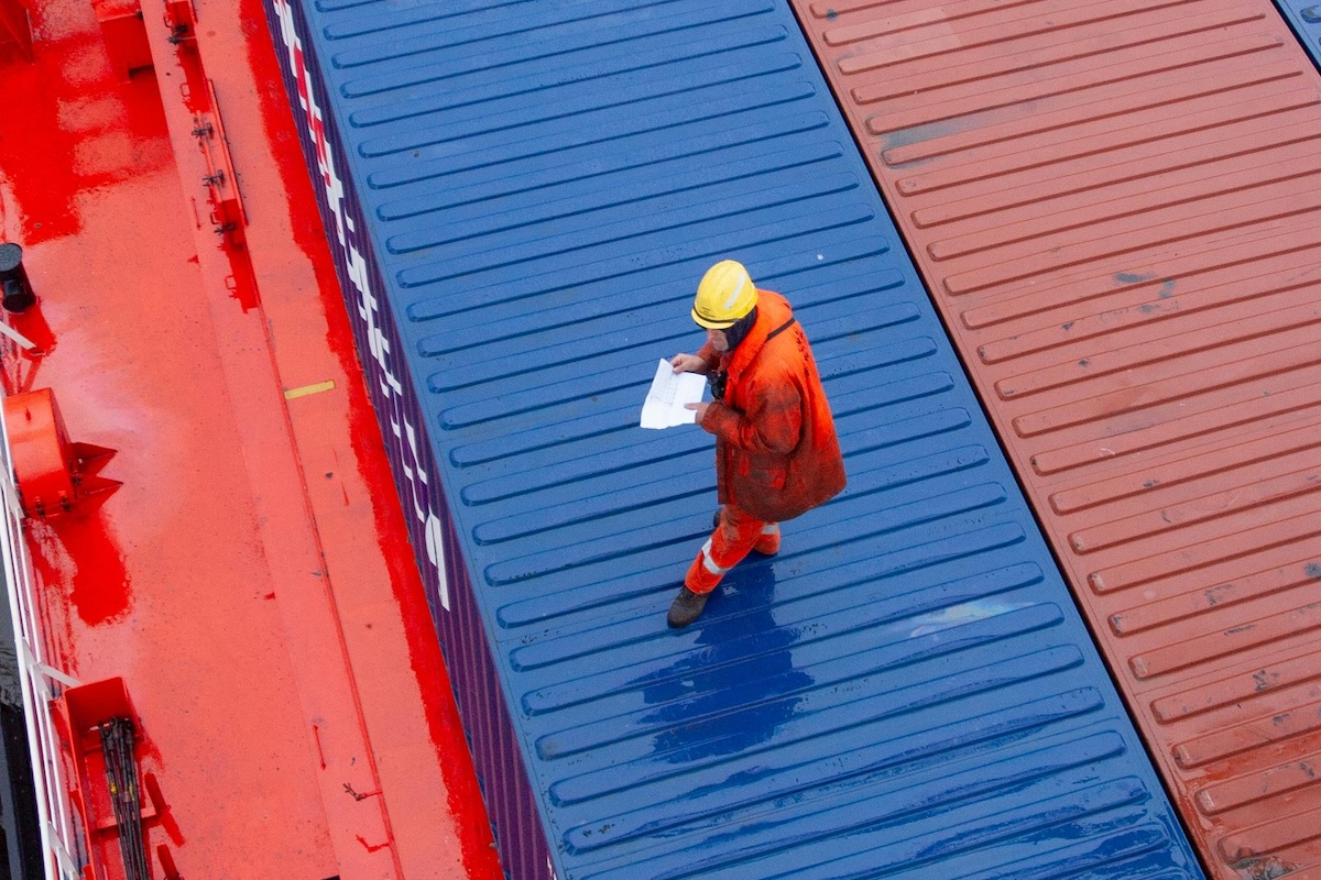 Overhead view of a worker inspecting containers on a ship deck in a maritime setting.