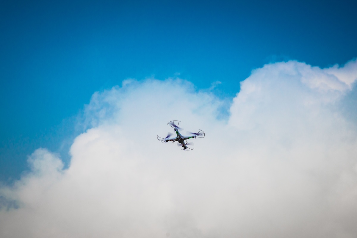 Drone flying against a vibrant blue sky with fluffy clouds, showcasing modern technology