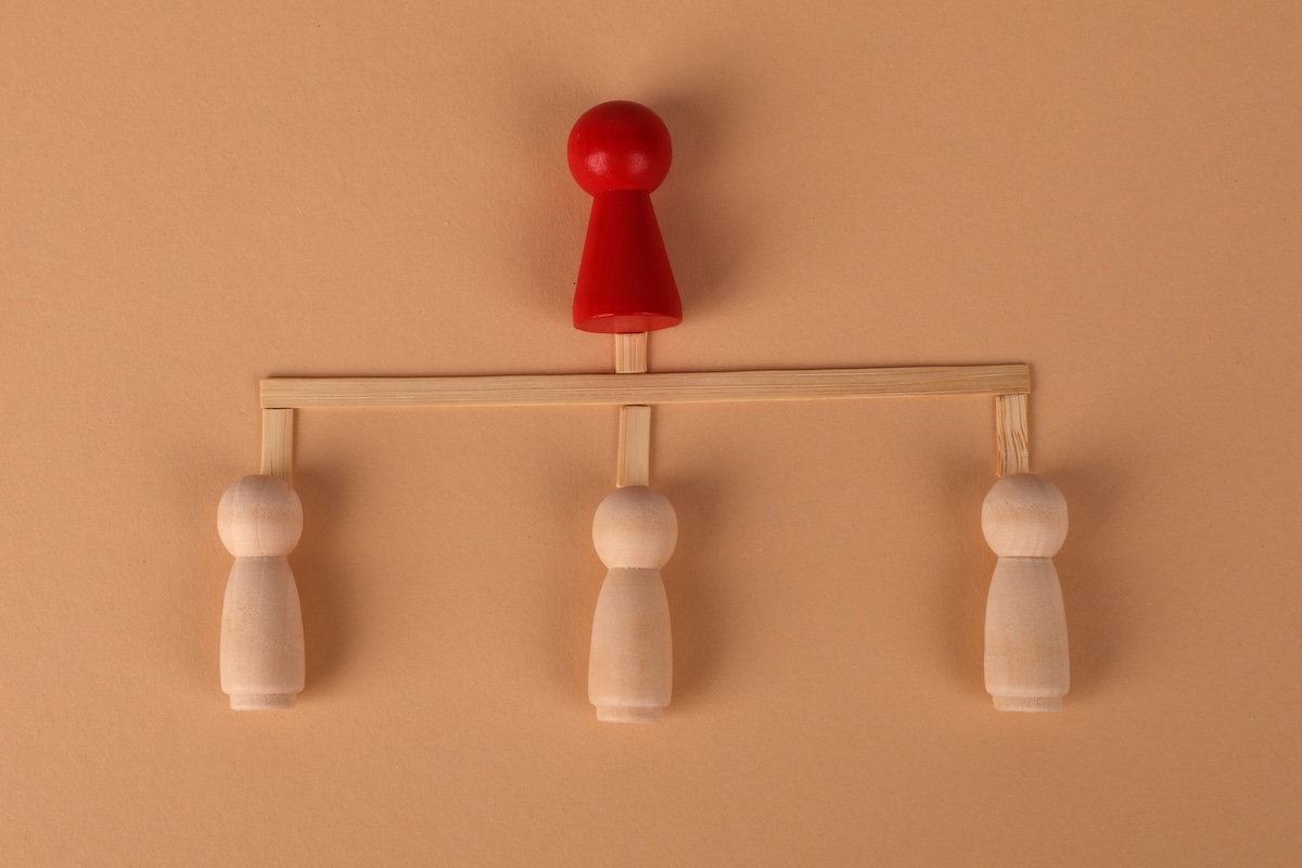 Minimalist arrangement of wooden figures depicting hierarchy and leadership concept.