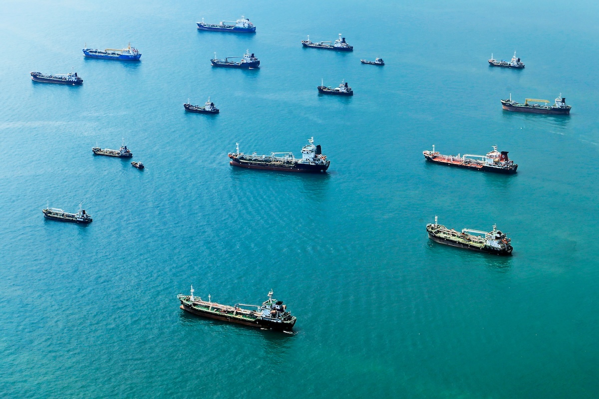 Numerous cargo ships anchored on the blue ocean, captured from above.