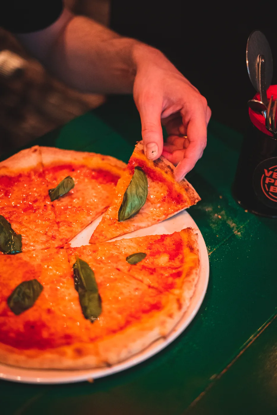 Een gast pakt een punt vegan pizza met basilicum bij Vegan Pizza Bar.