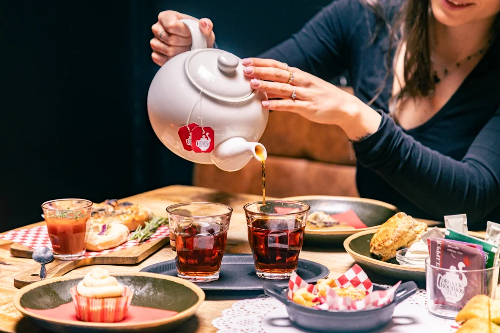 Tea being poured alongside scones and sweet pastries
