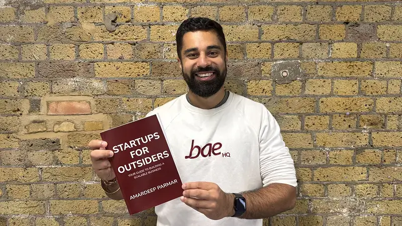 Amardeep Parmar standing with Startups for Outsiders book.