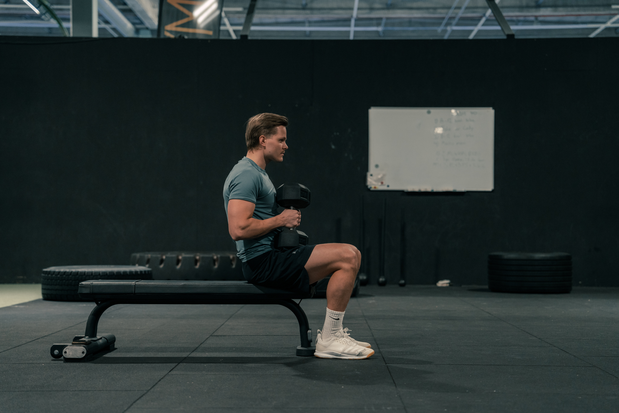 A lifter sits on a gym bench holding a dumbbell