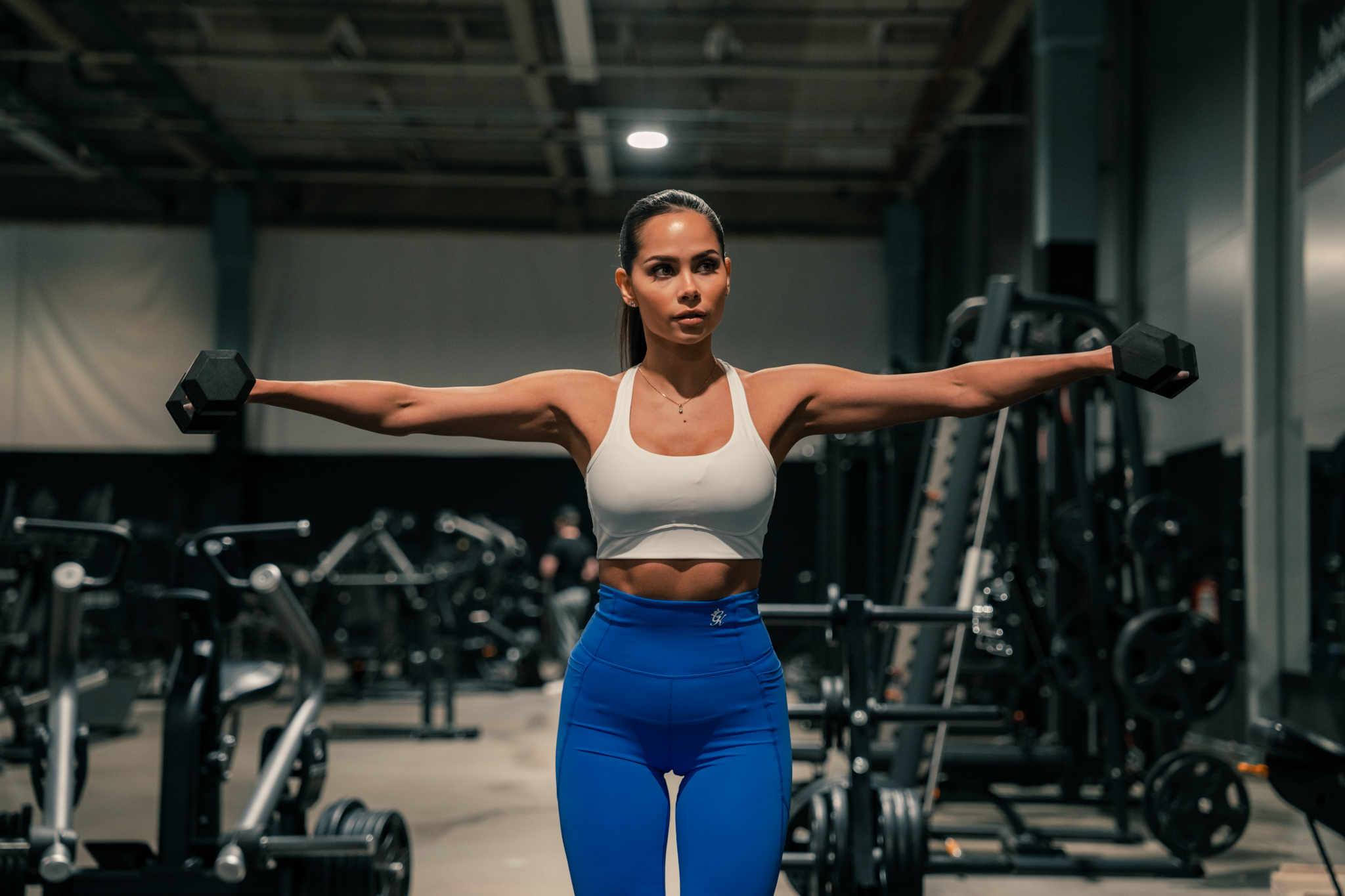 A person performing dumbbell lateral raises at the gym.