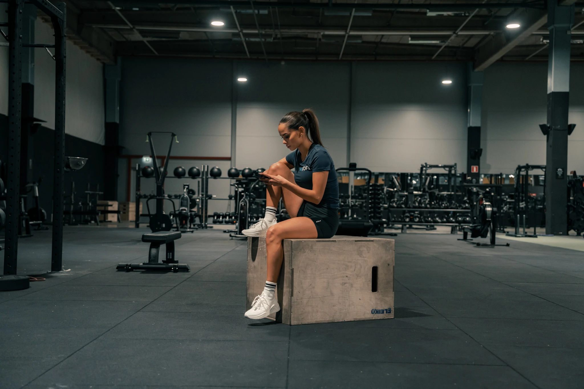 Kuvassa henkilö rentoutuu kuntosalilla setin välissä ja tarkistaa älypuhelintaan. Hän voi käyttää treenisovellusta seuratakseen harjoituksiaan ja parantaakseen treenien tehokkuutta.