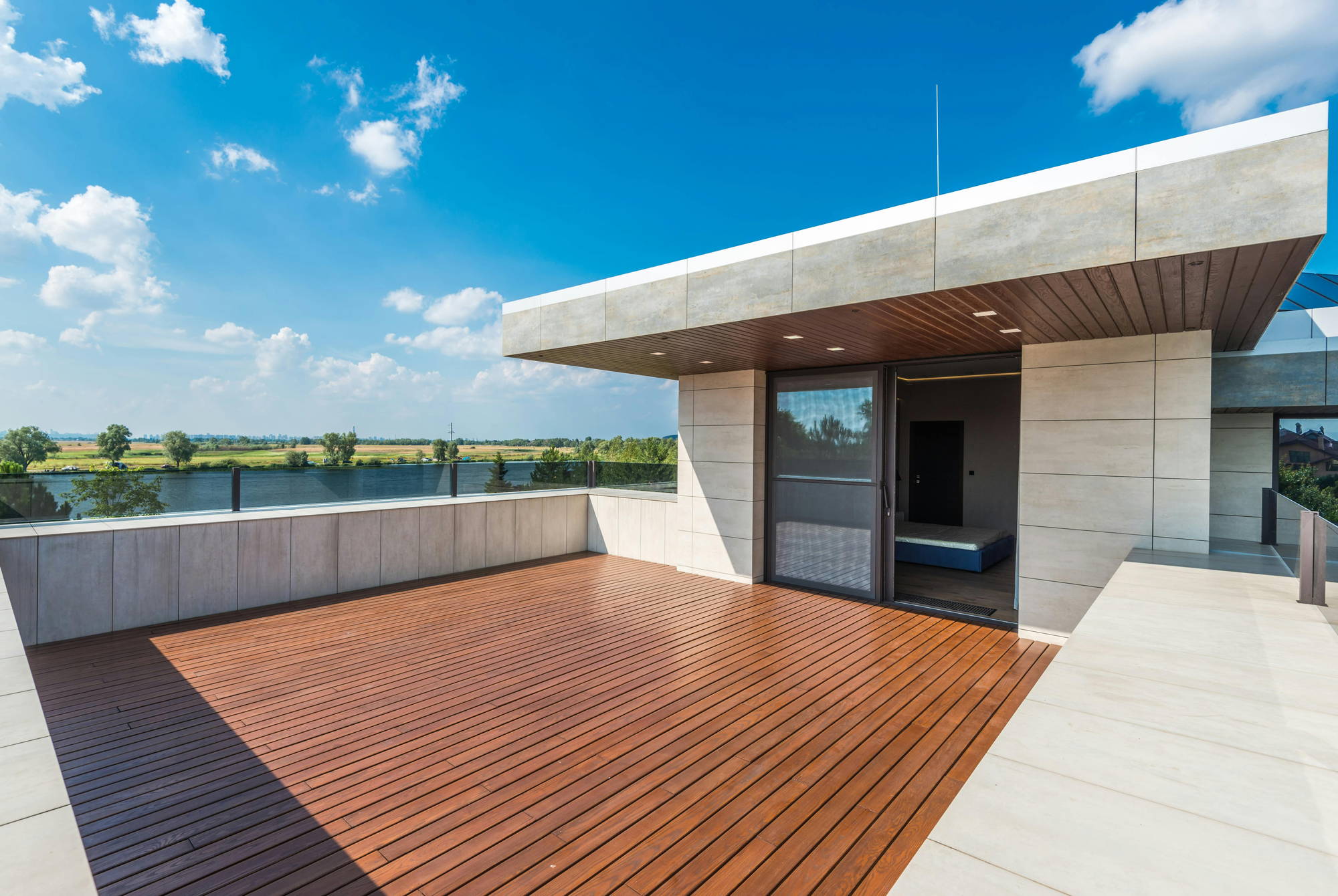 Empty rooftop terrace with a wooden deck, a concrete parapet and a river view, photographed for a real estate listing
