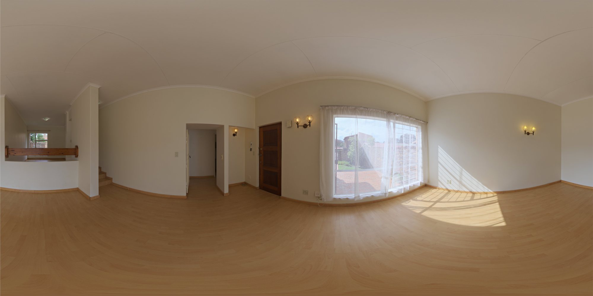 The same 360 degree living room panorama before staging, with bare wooden floors, a large curtained window, a wooden front door, a hallway and stairs