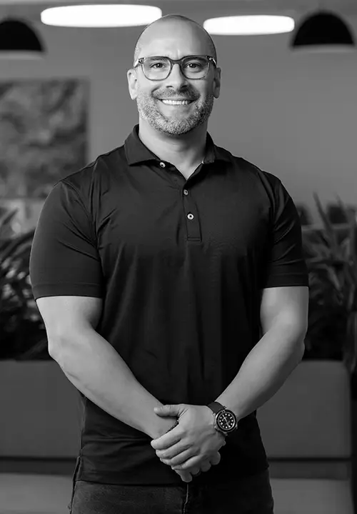 Founder, Brian Leffler, smiling wearing glasses and a black polo shirt standing with hands clasped indoors.